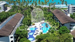 A resort with a central swimming pool, surrounded by palm trees and beachfront views. - Carneiros Beach Resort by CTA (Tamandaré)
