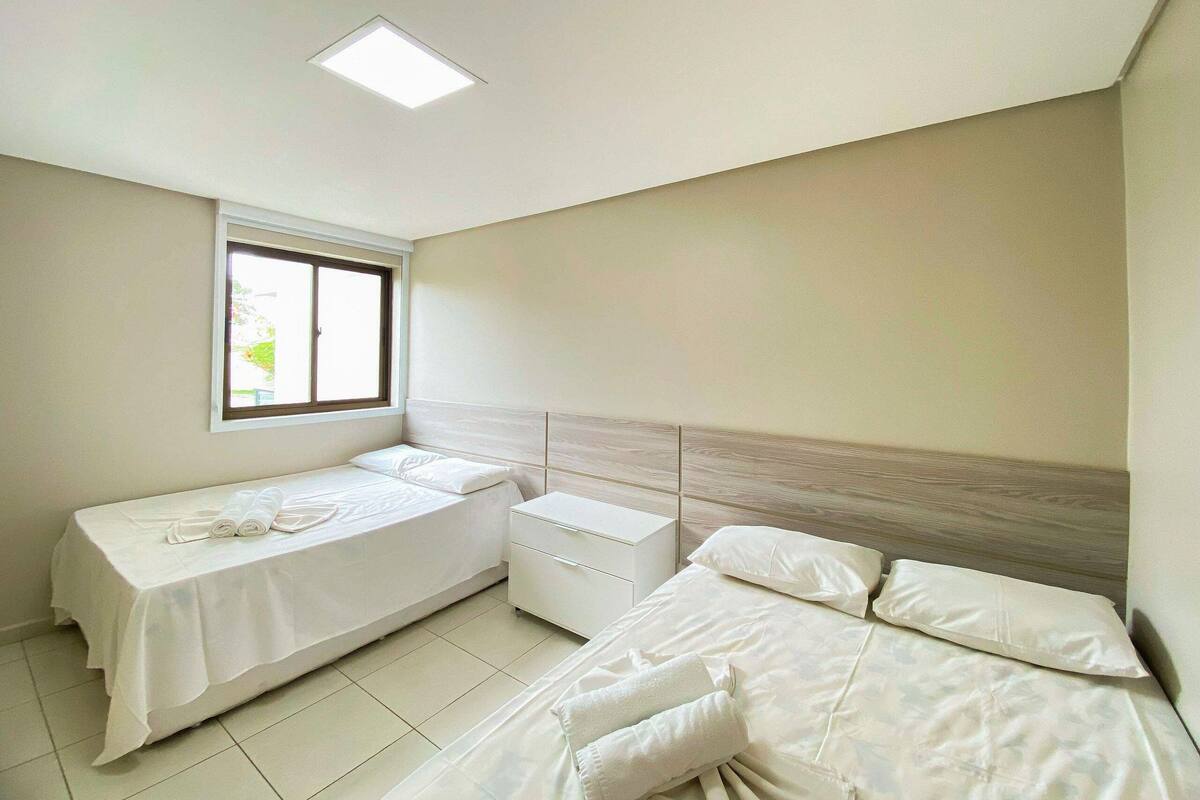 A bedroom with two beds, a window, a bedside table, and a ceiling light.