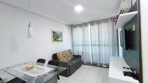 A living room with a glass table, a sofa, a painting on the wall, and a TV on the wall. - Carneiros Beach Resort by CTA (Tamandaré)