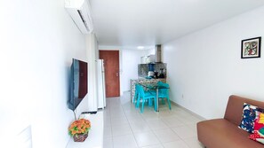 Un salon moderne avec un canapé, un téléviseur, un coin repas avec des chaises et une cuisine en arrière-plan.