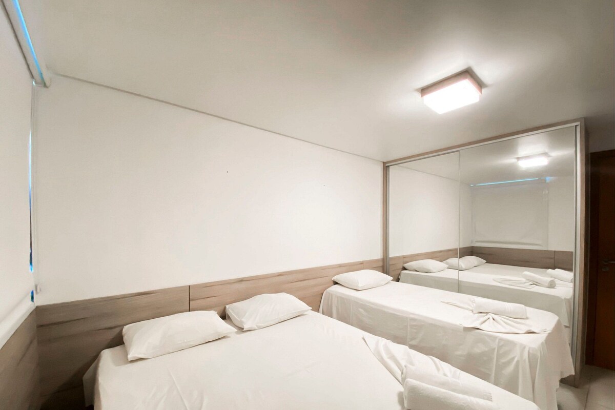 Una camera d'albergo con tre letti singoli, un grande specchio e una luce a soffitto.