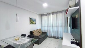 Ein Wohnzimmer mit Glastisch, einer Couch, einem Bild an der Wand und einem Fernseher.