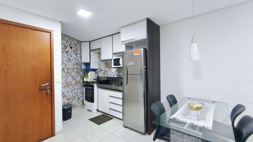 Cocina compacta con refrigerador, microondas y tostadora. Hay una mesa de comedor con sillas y un basurero pequeño.