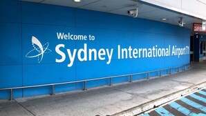 Een blauwe muur met de tekst 'Welcome to Sydney International Airport 11' en een vlinderlogo.