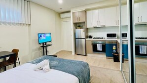 Een kleine hotelkamer met een bed, een televisie, een tafeltje en een kitchenette.