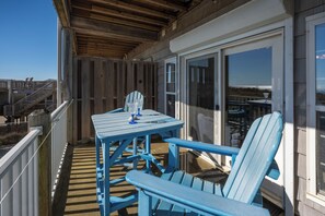 A covered outdoor deck with a table and chairs, a glass balustrade, and a view of the beach. - Oceanfront Condo, Beach Access, Shared Pool, & Hot Tub (Hatteras)