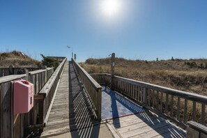 Ein hölzerner Steg führt zu einem Strand unter blauem Himmel.