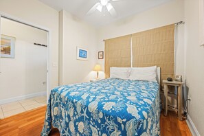 A bedroom with a bed, a bedside table, a lamp, and a window with curtains. - Oceanfront Condo, Beach Access, Shared Pool, & Hot Tub (Hatteras)