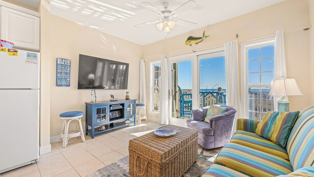 A living room with a television, a sofa, a coffee table, and a balcony with a view. - Oceanfront Condo, Beach Access, Shared Pool, & Hot Tub (Hatteras)