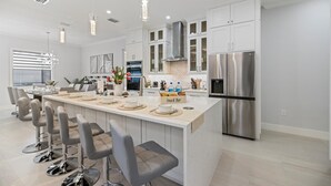 Une cuisine moderne avec des meubles blancs, des appareils en acier inoxydable et un îlot central doté de tabourets de bar.