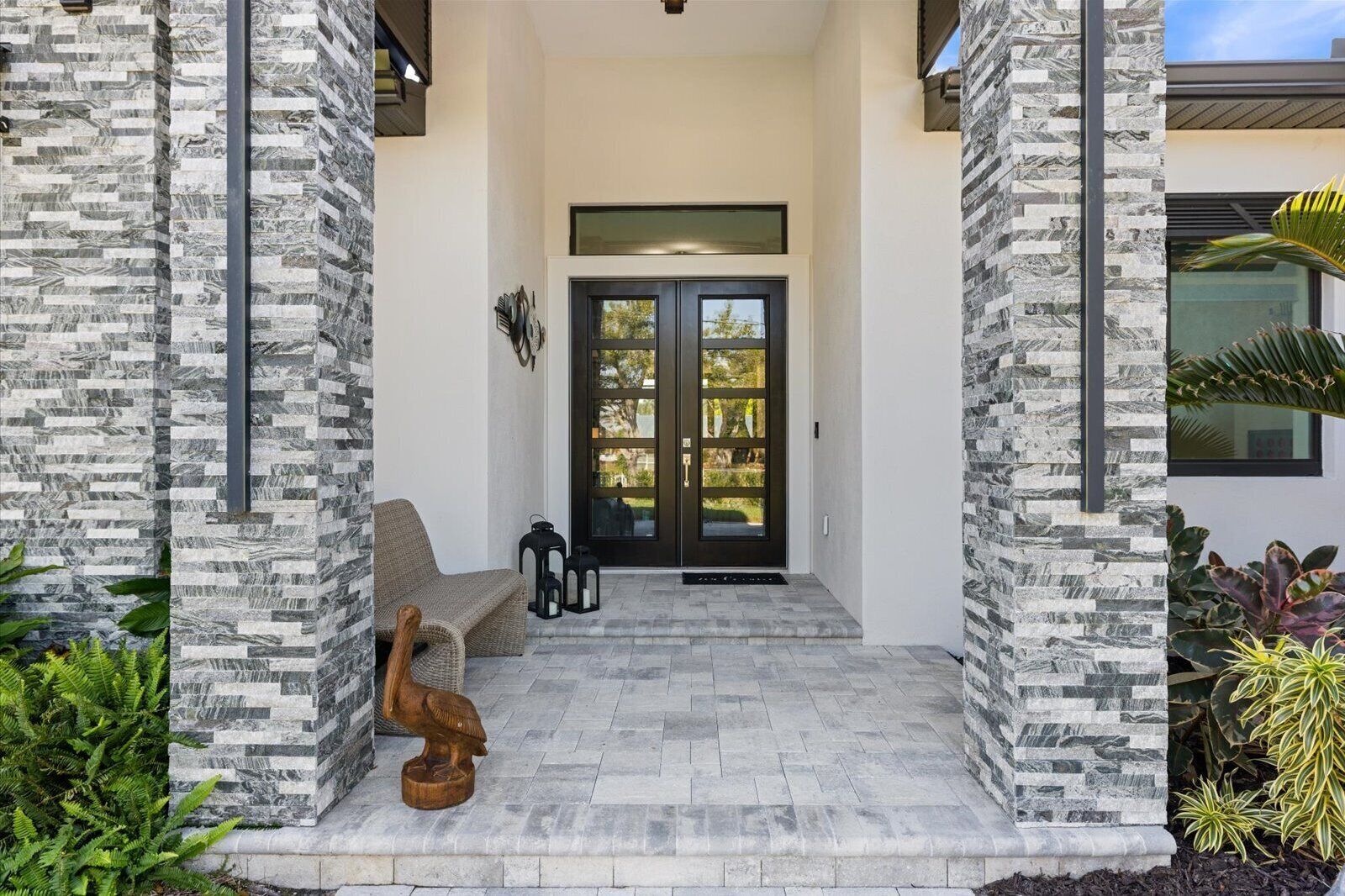 Une entrée moderne avec une façade en pierre, une porte double de couleur sombre et un banc à l’extérieur.