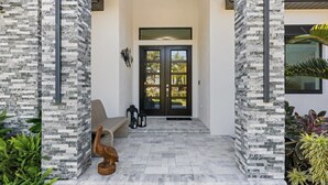 Une entrée moderne avec une façade en pierre, une porte double de couleur sombre et un banc à l’extérieur.