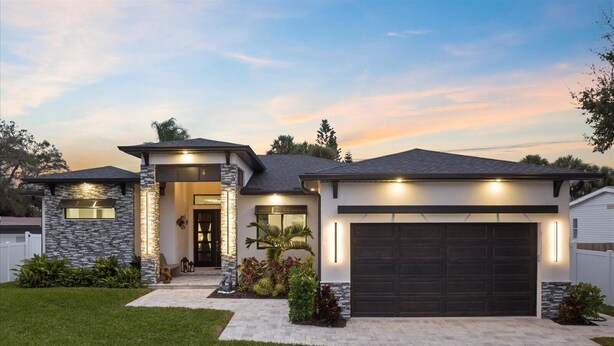 Une maison moderne à deux étages, dotée d’une façade en pierre, d’une porte de garage sombre et d’une pelouse bien entretenue.