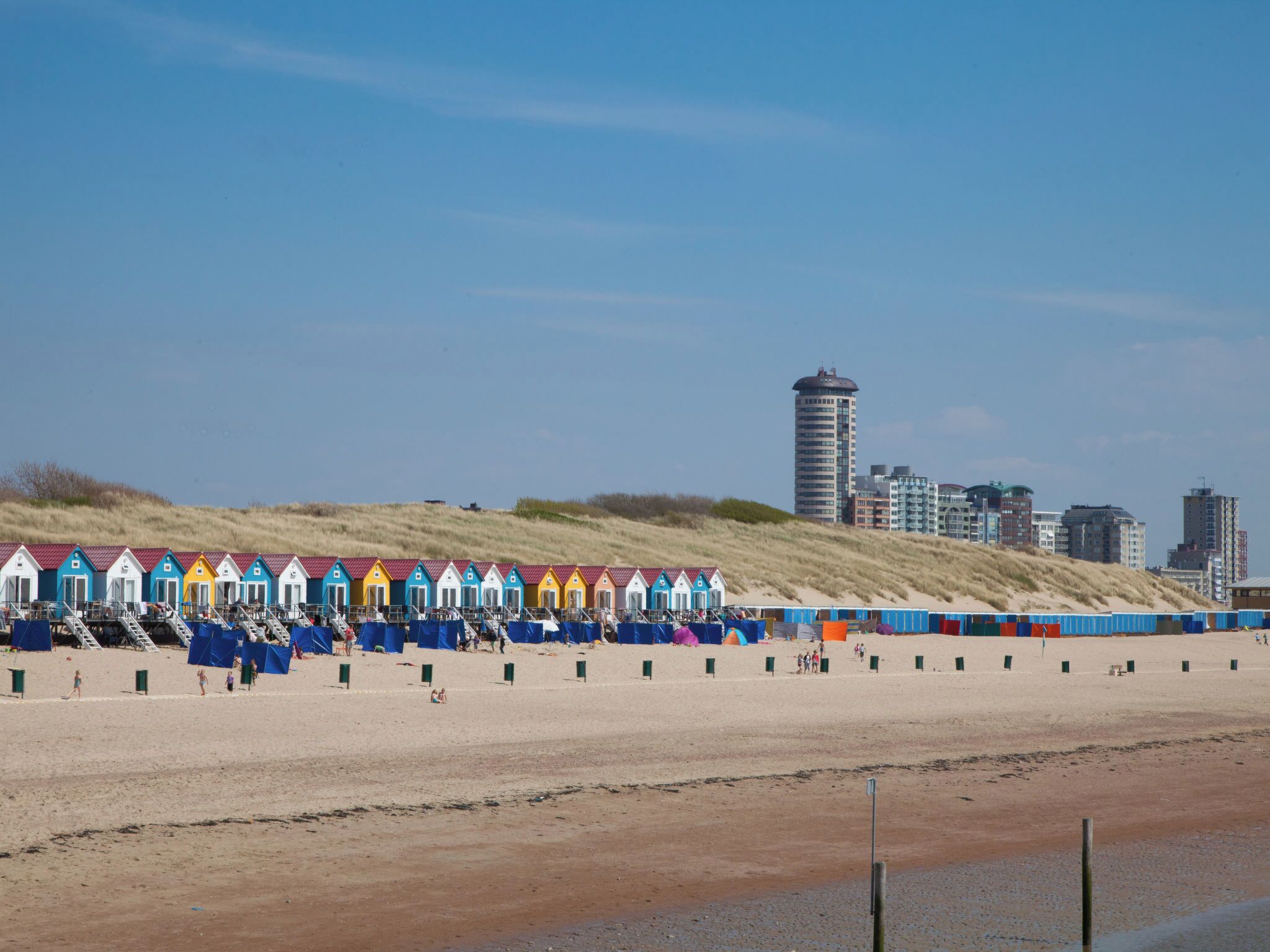 Een strand met kleurrijke strandhutten en een stadsgezicht op de achtergrond.
