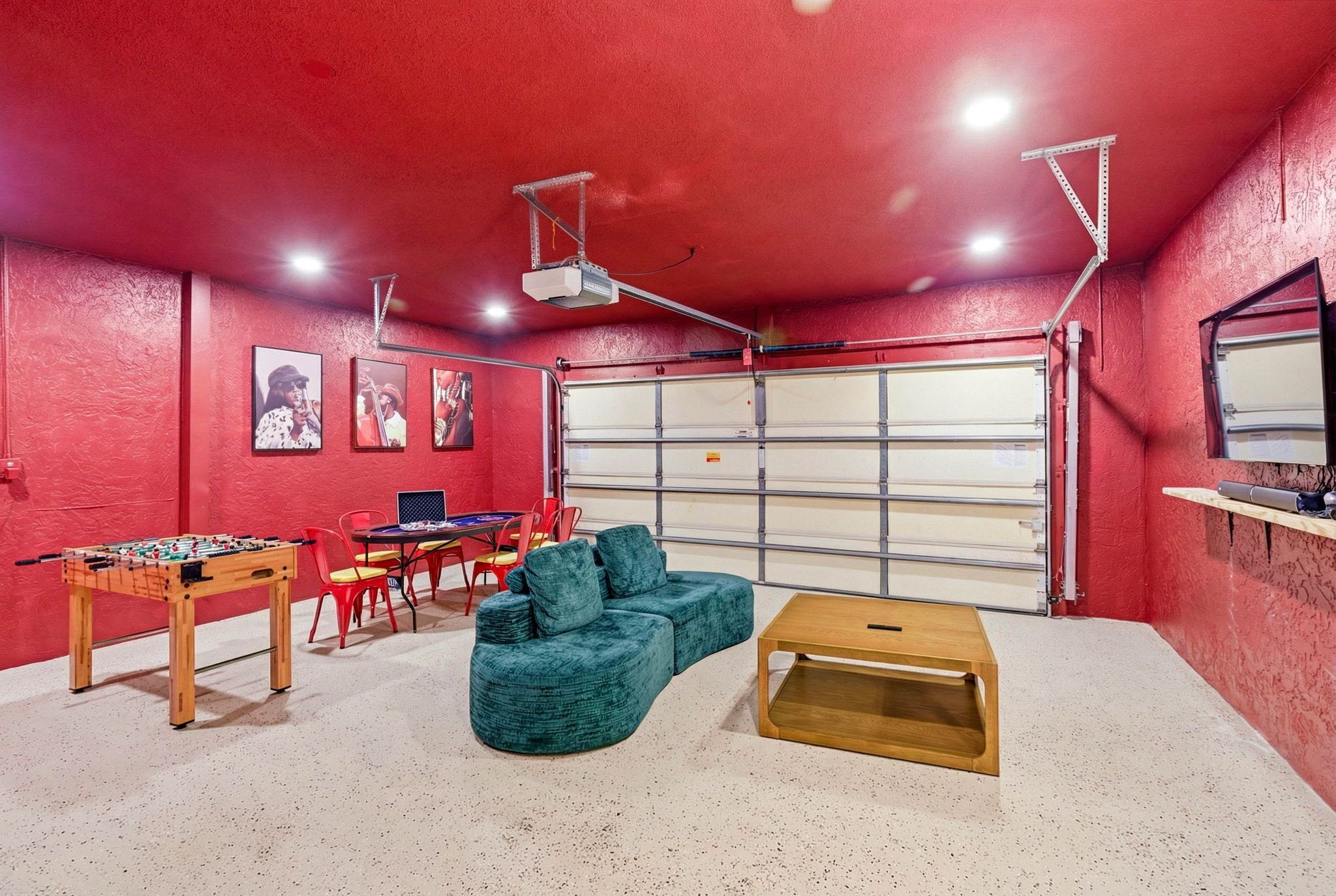 A room with a red wall, a foosball table, a blue sofa, a wooden coffee table, and a garage door.