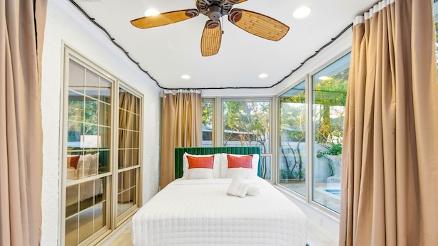 Une chambre dotée d’un grand lit, d’un ventilateur de plafond et offrant une vue sur l’extérieur.
