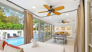 Une chambre d’hôtel avec un lit, deux ventilateurs de plafond, une vue sur une piscine et un coin repas avec une table et des chaises.