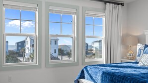 Une chambre à coucher avec un grand lit, trois fenêtres et une vue sur des maisons.