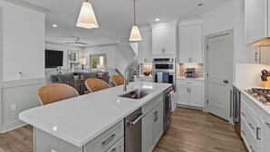 Une cuisine moderne avec des meubles blancs, des appareils en acier inoxydable et un îlot central doté de sièges.