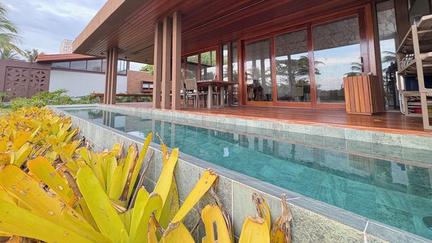 A modern poolside area with a wooden deck, large windows, and a clear pool. - Alma Maraú  (Maraú)