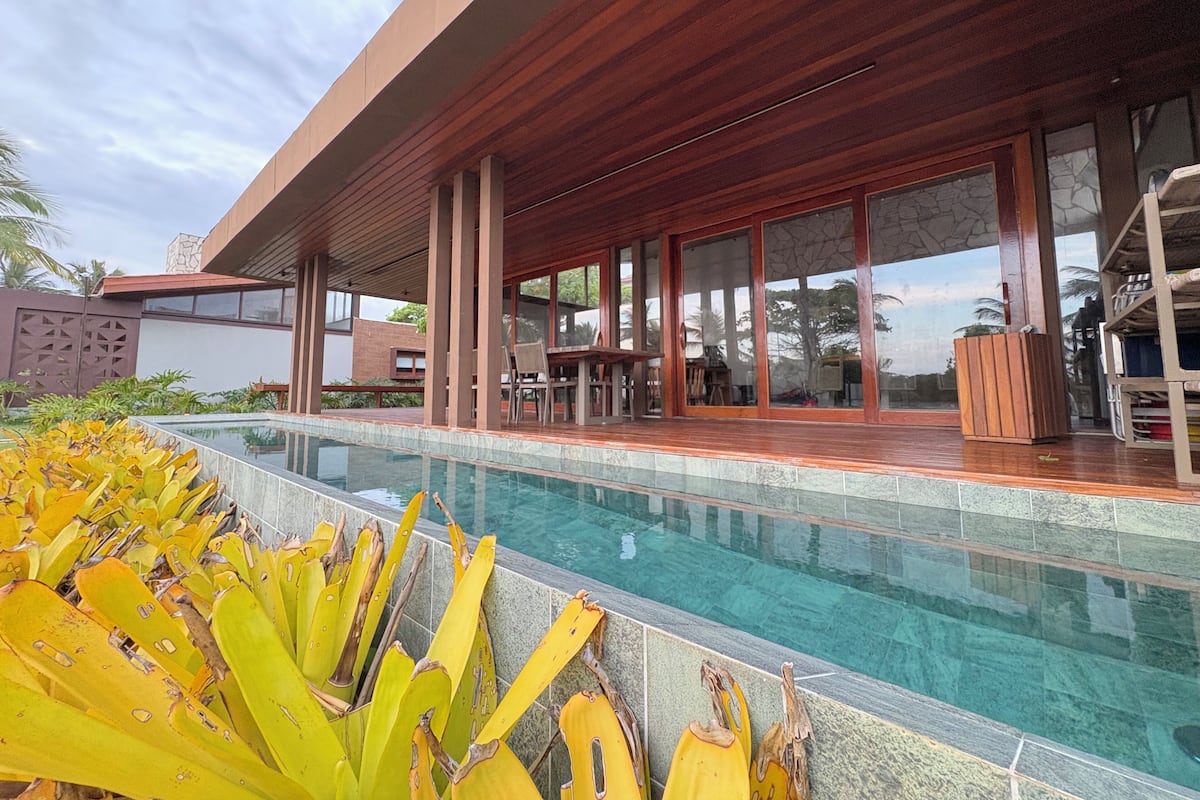 A modern poolside area with a wooden deck, large windows, and a clear pool.