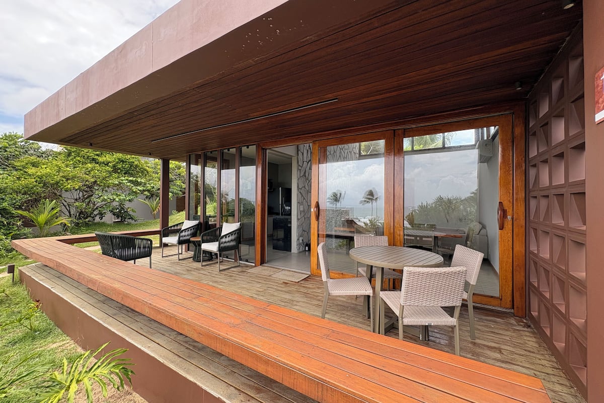 A modern outdoor patio with wooden decking, glass doors, and wicker furniture.