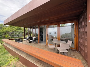A modern outdoor patio with wooden decking, glass doors, and wicker furniture. - Alma Maraú (Maraú)