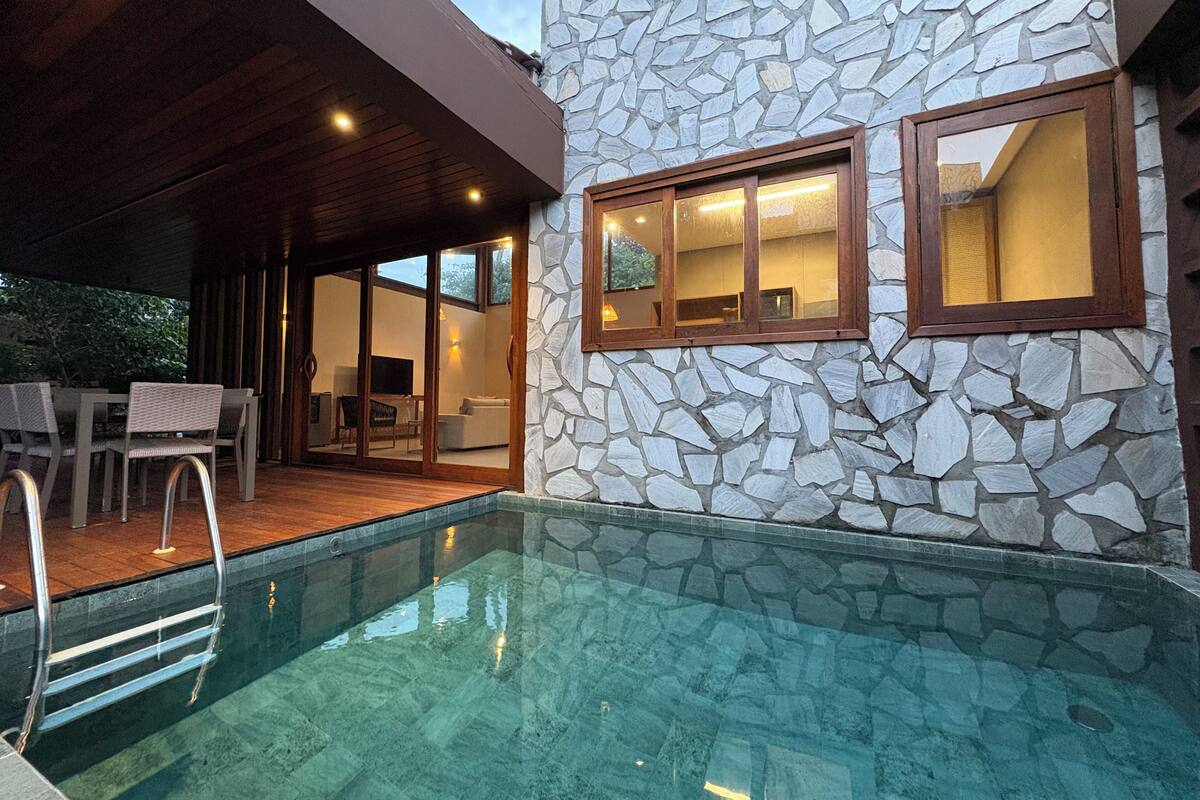 A modern pool area with stone walls, a wooden deck, and a glass-enclosed lounge.