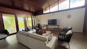 A modern living room with a sofa, chairs, a coffee table, a TV, and a balcony with large windows. - Alma Maraú  (Maraú)