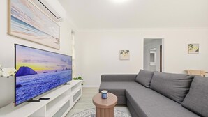 Ett vardagsrum med en platt-TV, en grå soffa och ett litet runt bord.