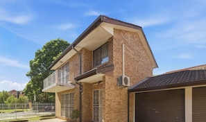 A two-story house with a balcony, a garage, and a brick exterior. - Cabramatta | Spacious 3 Bedroom Family Townhouse (Cabramatta)