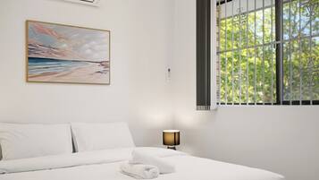 A hotel room with a bed, a painting, a window with bars, and a lamp.