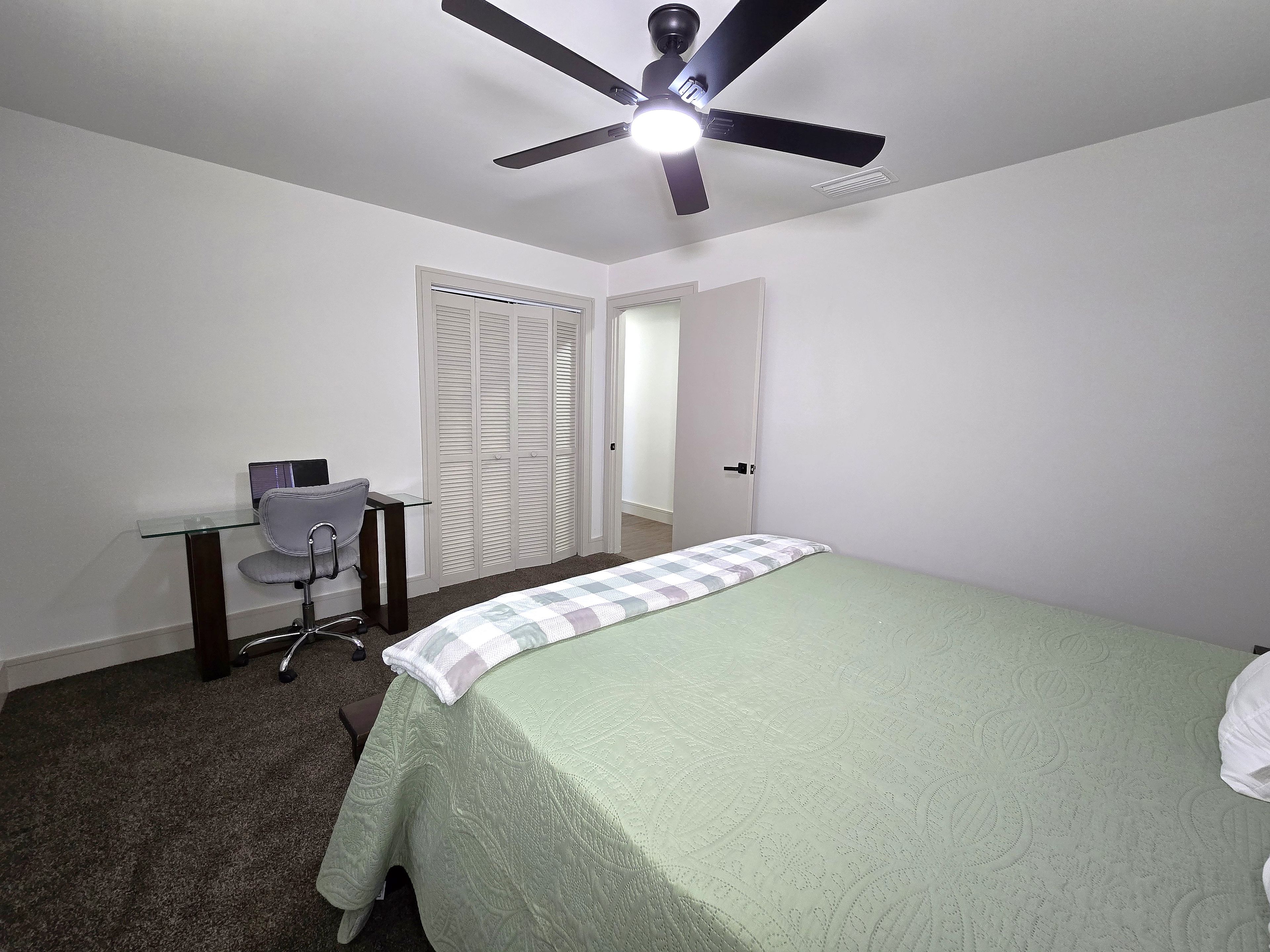 A bedroom with a bed, a desk, a chair, a wardrobe, and a ceiling fan.