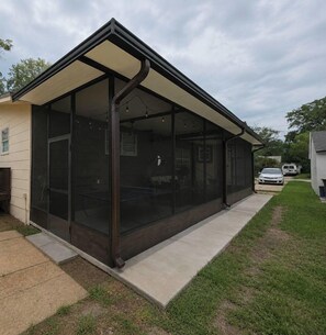 A covered patio with a glass enclosure, a concrete pathway, and a lawn area. - Historic Avondale 5BR | Porch, Grill & Parking (Jacksonville)