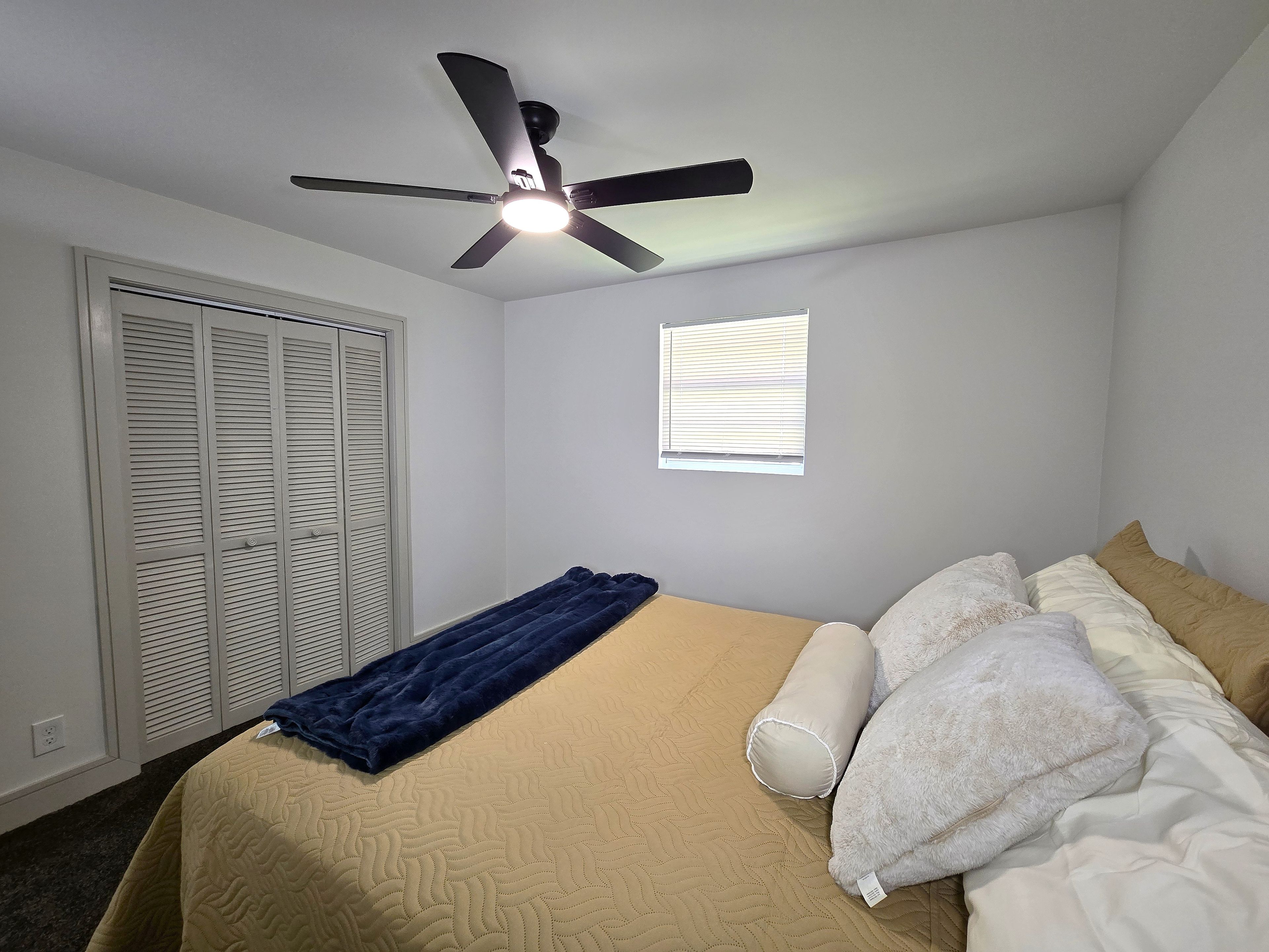 Une chambre à coucher avec un lit, un ventilateur de plafond, une fenêtre et un placard.