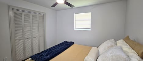 Un dormitorio con cama, ventilador de techo, ventana y armario.