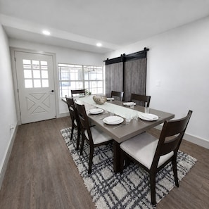 Comedor con una mesa rectangular dispuesta para cuatro personas, rodeada de sillas de madera oscura con cojines de color claro.