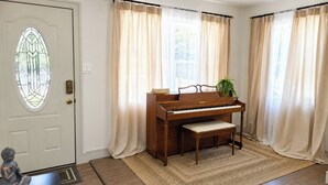 Ett piano i ett rum med en dörr, gardiner och en matta.