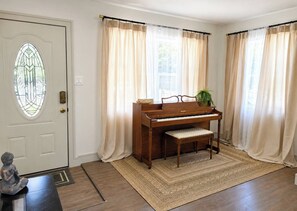 Ein Klavier in einem Raum mit Tür, Vorhängen und Teppich.
