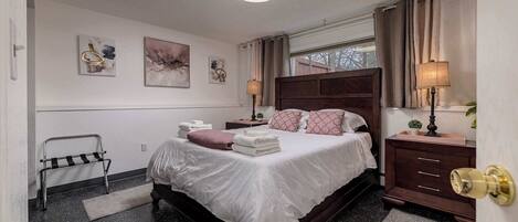 Un dormitorio ordenado con una cama grande, mesitas de noche, una lámpara y obras de arte en las paredes.