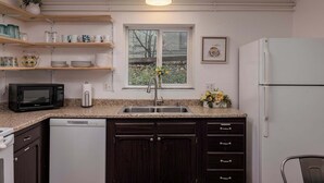 Una cocina equipada con lavavajillas, microondas, pileta y refrigerador. Hay estantes sobre la pileta con diversos objetos, y una ventana sobre la pileta.