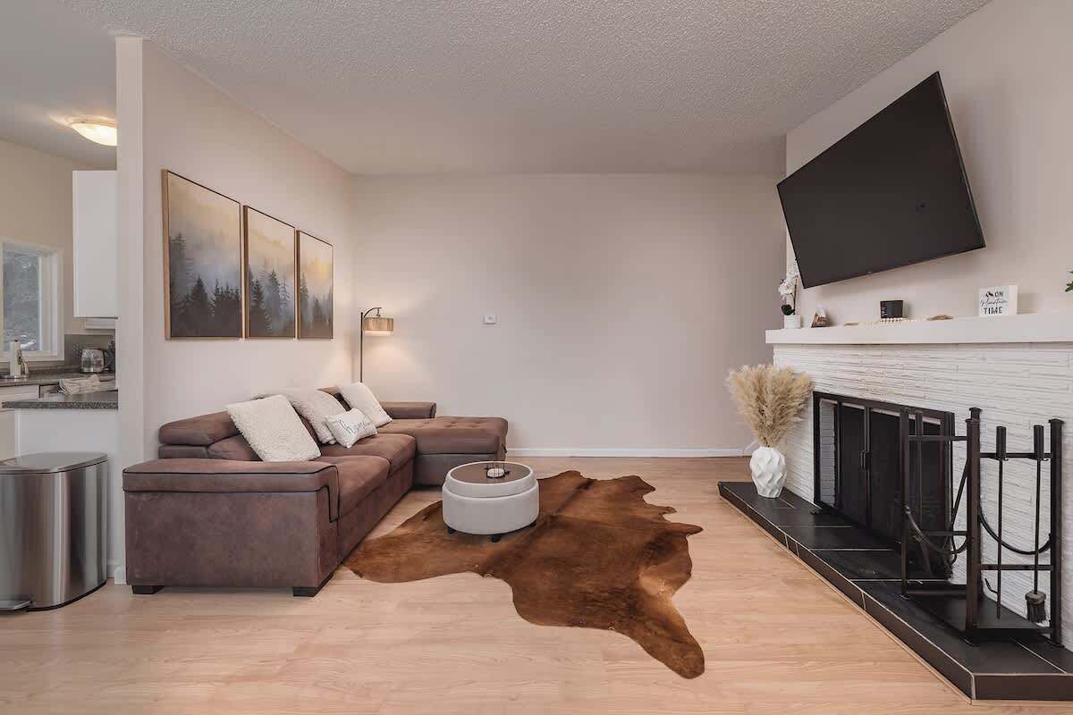 Un salon moderne avec un canapé d’angle, une table basse ronde, un téléviseur fixé au mur et une cheminée.