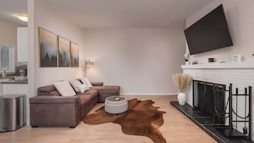 Un salon moderne avec un canapé d’angle, une table basse ronde, un téléviseur fixé au mur et une cheminée.