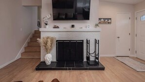 A modern living room with a fireplace, a mounted TV, and a staircase leading to another level. - Cozy South Addition Downtown Getaway - King Beds (Anchorage)