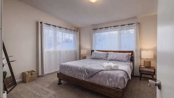 Une chambre à coucher bien rangée, avec un grand lit, deux tables de chevet avec des lampes et une fenêtre avec des rideaux.