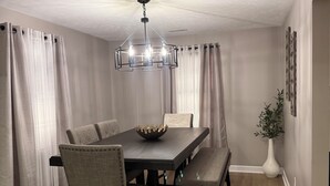A dining area with a dark wooden table, four chairs, a chandelier, and a vase with a plant.