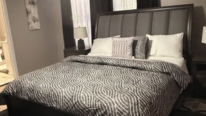 A bedroom with a bed, a ceiling fan, a nightstand with a lamp, and a window with curtains.