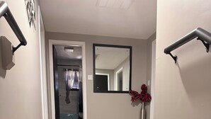 A hallway with a black rug, wooden flooring, a mirror, and a vase with red flowers.