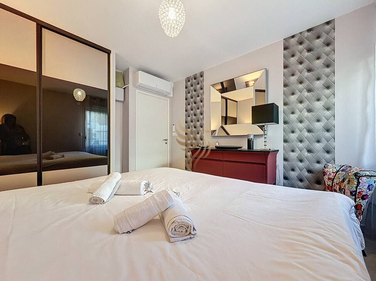 A hotel room with a large bed, a mirror, a tufted headboard, a red dresser, and a window with curtains.