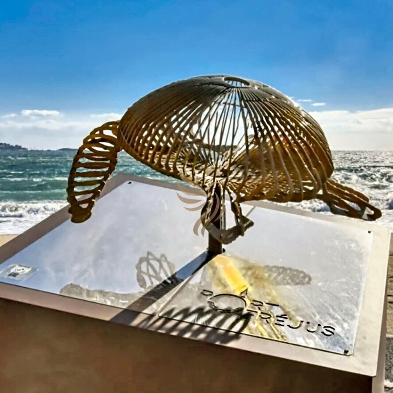 A metal sculpture of a sea turtle on a glass table with a coastal view.
